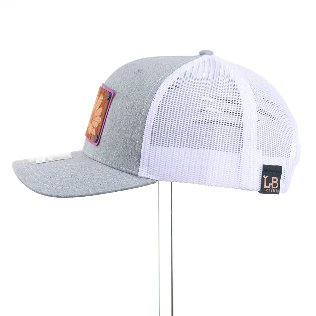 Gray and white trucker hat with mesh back on a white background featuring a wood and metal patch with an etching of a Bitterroot flower
