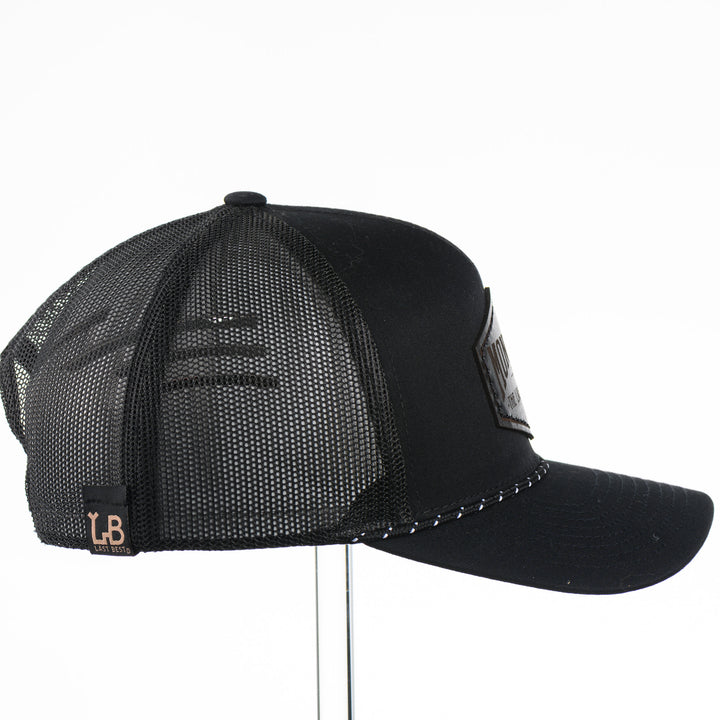 Black trucker cap side view with a black leather patch that says Montana The Last Best Place