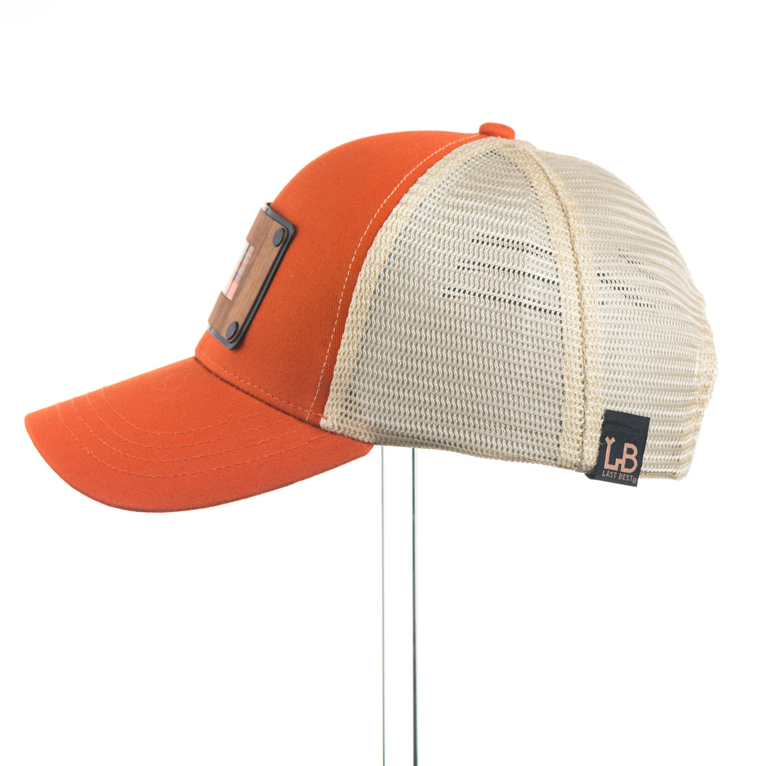 Orange and beige trucker cap with mesh back on a white background featuring a wood and copper patch of Montana