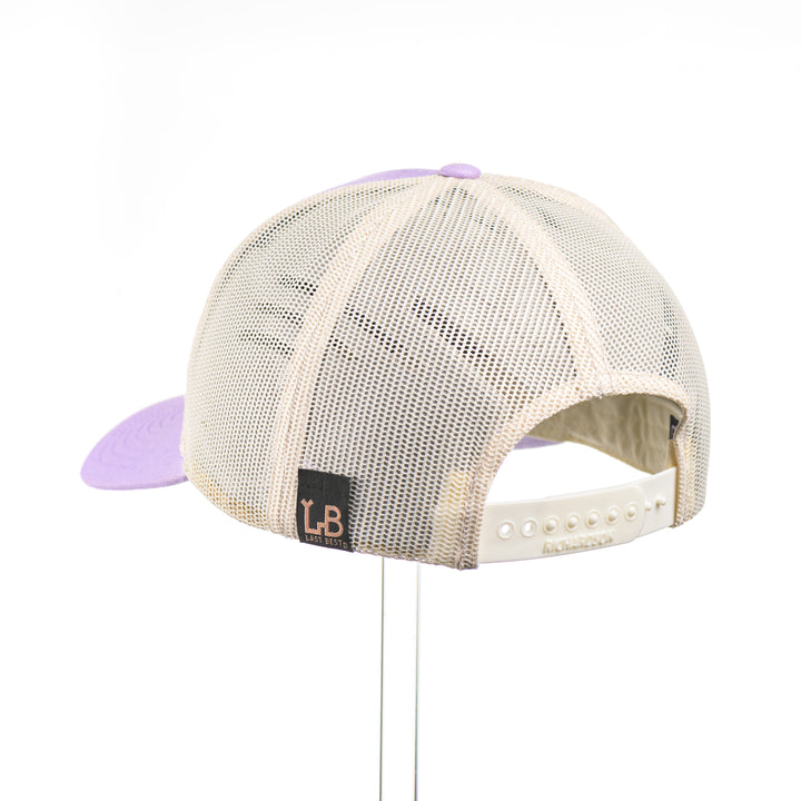 Cherry Wood Bitterroot Flower Patch Lilac & Cream Trucker Hat, featuring a real cherry wood veneer patch etched with a bitterroot flower, laminated to a light purple anodized aluminum plate and riveted to a lilac and cream trucker hat along—handmade in Montana, USA by Last Best Supply Co.