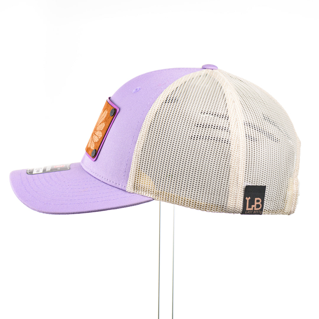 Cherry Wood Bitterroot Flower Patch Lilac & Cream Trucker Hat, featuring a real cherry wood veneer patch etched with a bitterroot flower, laminated to a light purple anodized aluminum plate and riveted to a lilac and cream trucker hat along—handmade in Montana, USA by Last Best Supply Co.