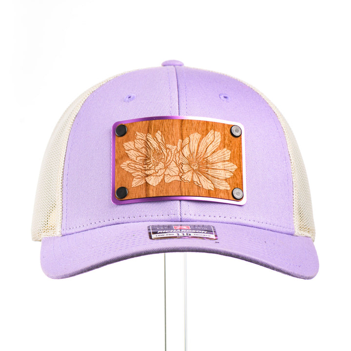 Cherry Wood Bitterroot Flower Patch Lilac & Cream Trucker Hat, featuring a real cherry wood veneer patch etched with a bitterroot flower, laminated to a light purple anodized aluminum plate and riveted to a lilac and cream trucker hat along—handmade in Montana, USA by Last Best Supply Co.