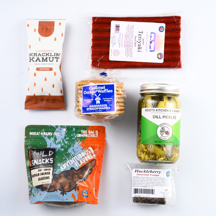 A Montana made snack gift box called The Last Best Box featuring teriyaki beef sticks, classic dill pickles, caramel cookie waffles, huckelberry fudge, buffalo soldier cashews and churro kracklin kamut.