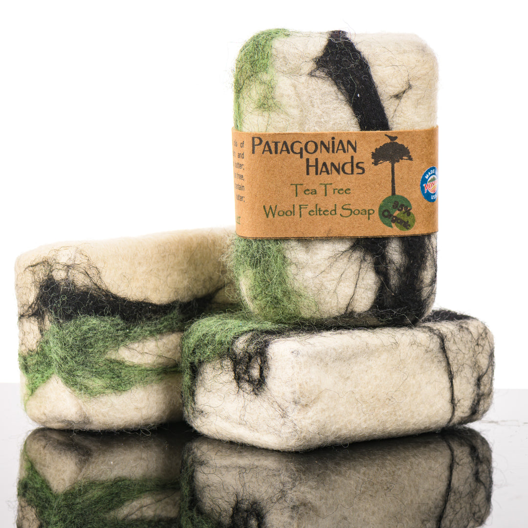 Three pieces of Patagonian Hands Tea Tree Wool Felted Soap on a reflective surface with a white background