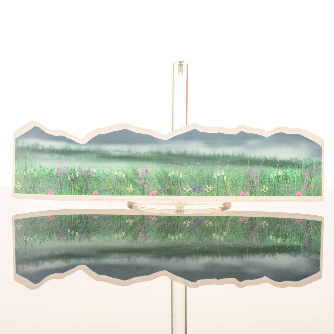 A long sticker of a mountain scape with a wildflower field painted by Montana artist Creatively Leanne, featured in The Petals to Peaks Box by The Last Best Box.