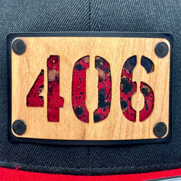 A  Close up of a flex fit, black and red flat bill hat with a wood and metal patch featuring 406, for the Montana area code, and red copper inlay.
