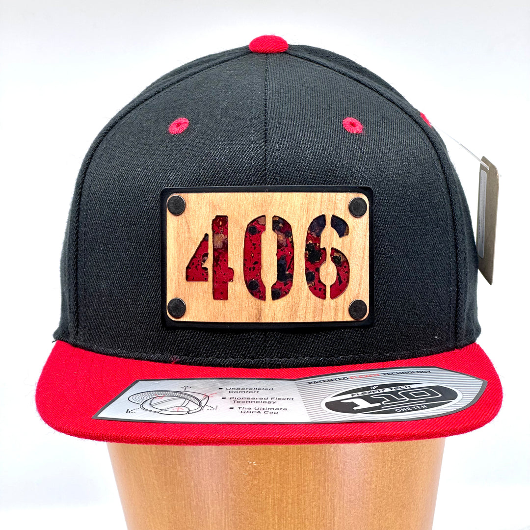 A flex fit, black and red flat bill hat with a wood and metal patch featuring 406, for the Montana area code, and red copper inlay.