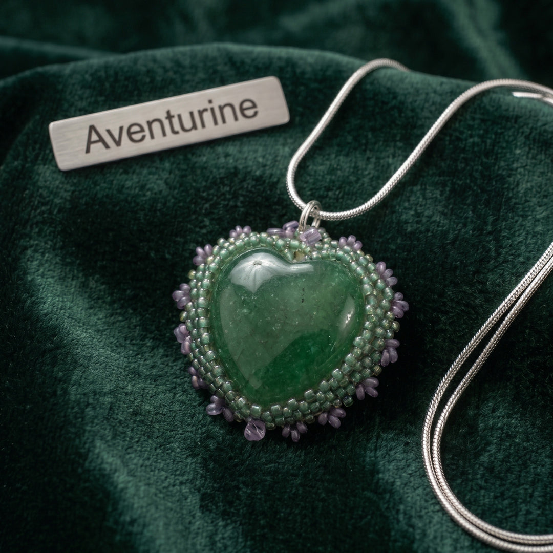 Heart-shaped aventurine pendant with beaded edge on green fabric, labeled &