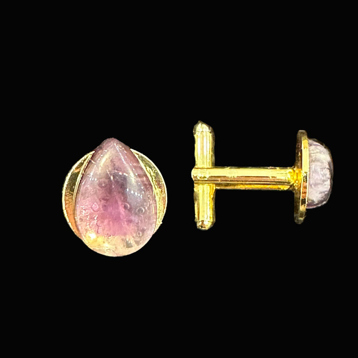 Gold cuff links with amethyst gemstones on a black background