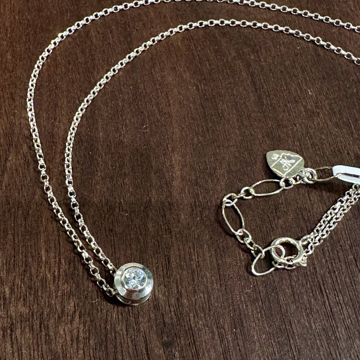 A cubic zirconia gemstone looking like a sparkling diamond for an April Birthstone Necklace, set in sterling silver on a dark wood background