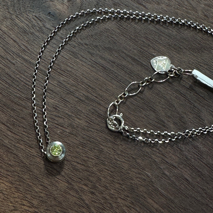 A cubic zirconia gemstone colored sparkling Peridot green for an August Birthstone Necklace, set in sterling silver on a dark wood background