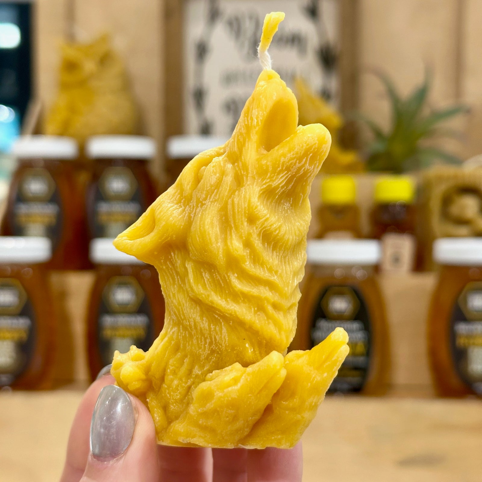 A view of the detail on a golden 100% Montana beeswax candle of a wolf howling with the heads of the wolfpack below it.
