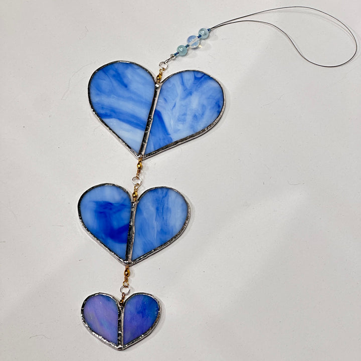 A stained glass suncatcher with three blue marbled glass heart panels with a blue beaded cord 