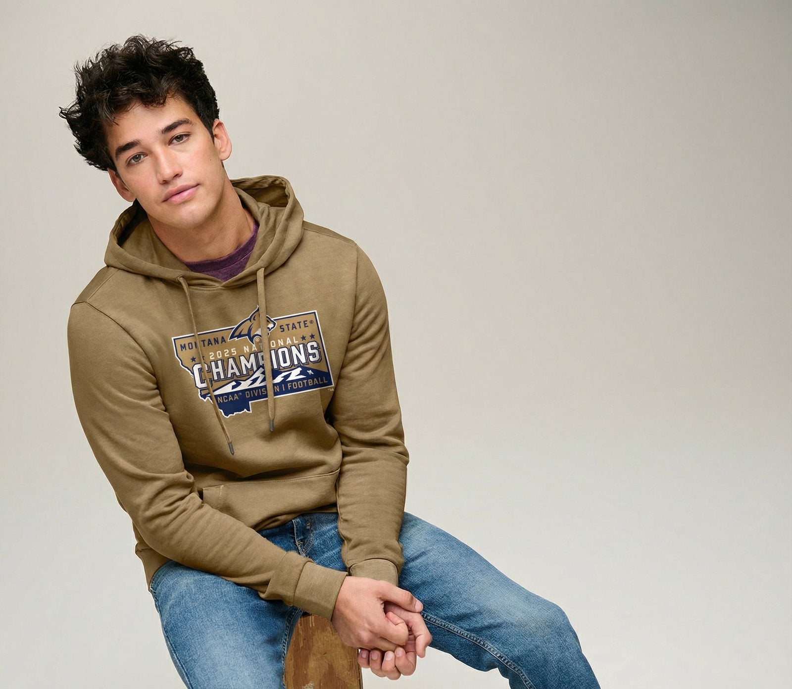 Person wearing a Beige Bobcats National Champions 2025 Wash Fleece Hoodie with bold blue, white, and gold Montana State 2023 National Champions graphic, made in Montana (home of the MSU Bobcats)