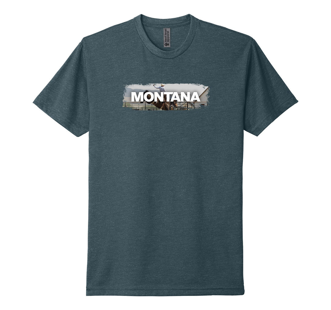 Indigo blue Next Level Apparel unisex adult tee featuring the official MT Department of Commerce ‘Montana’ lettering over the image of a cowboy astride a bucking bronco, designed and printed in Montana by Blue Peak Creative