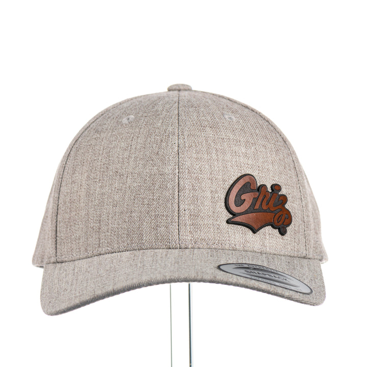 Front of a Tiny Leather Griz Script - Premium Wool Blend Cap—a heather grey premium wool blend snapback hat with a small brown leather Griz Script patch, made in Missoula, Montana (home of the UM Grizzlies) by Blue Peak Creative