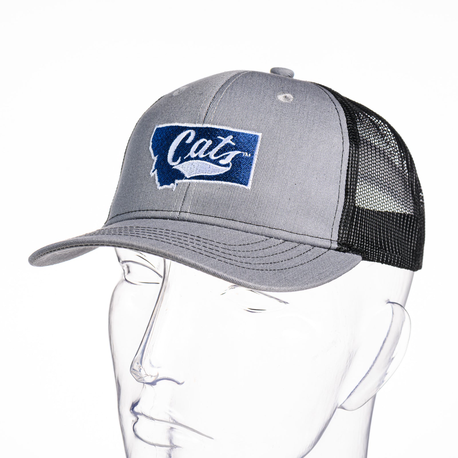 3/4 view of a grey and black Cats Montana Youth Snapback Trucker Hat made in Montana (home of the MSU Cats) by Blue Peak Creative—a grey and black youth trucker hat embroidered with a white Cats script over a blue Montana state silhouette, outlined in white