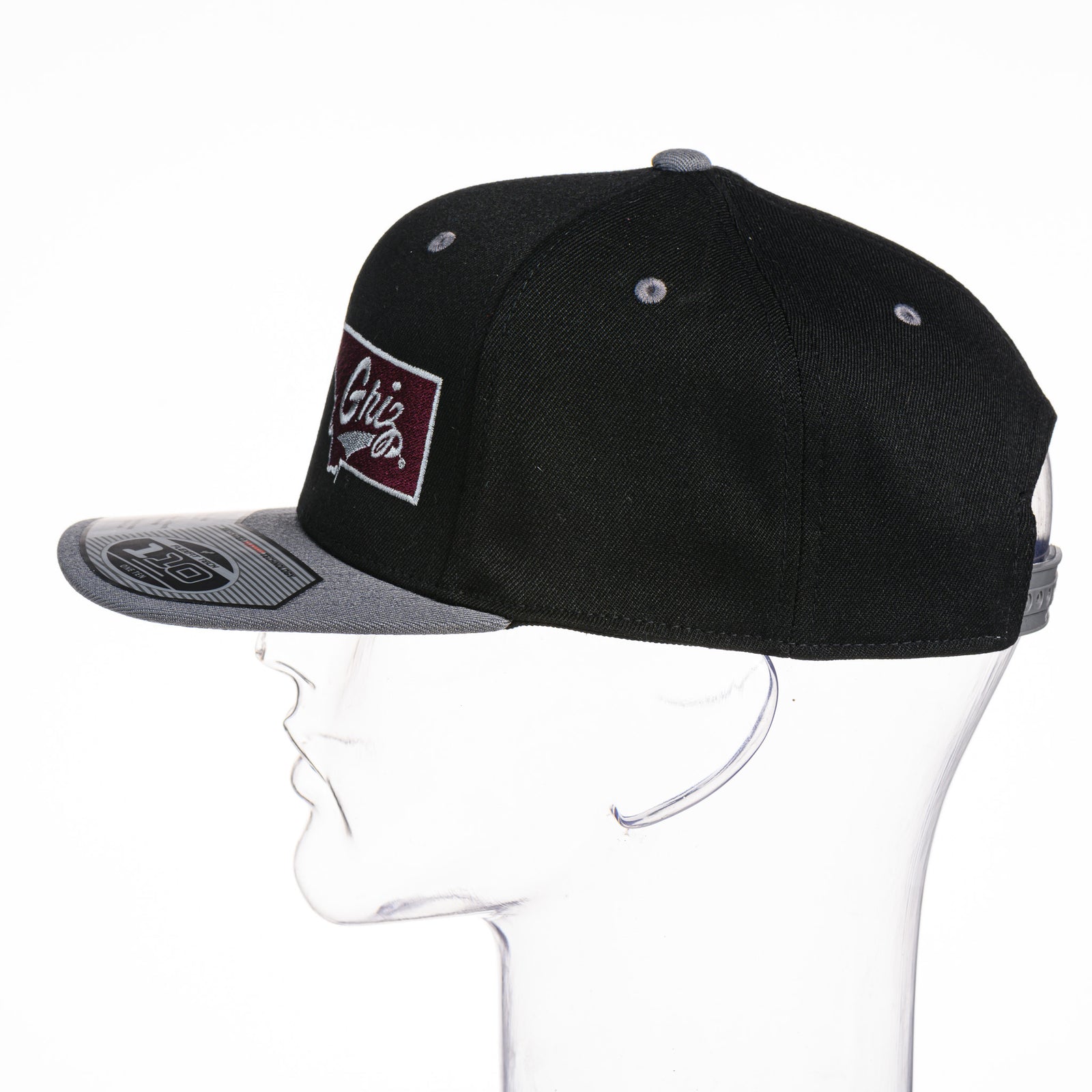 Black Montana Griz Script - Flat Bill Hat made in Missoula, MT (home of the UM Grizzlies) by Blue Peak Creative—a black flat bill hat embroidered with the University of Montana Griz script inside the outlined silhouette of the state of Montana (side).