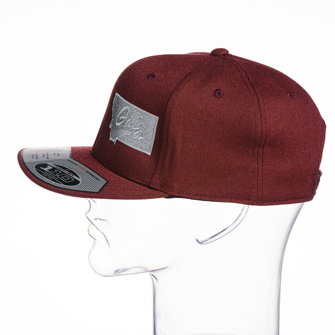 Maroon Montana Griz Script - Flat Bill Hat made in Missoula, MT (home of the UM Grizzlies) by Blue Peak Creative—a maroon flat bill hat embroidered with the University of Montana Griz script inside the outlined silhouette of the state of Montana (side).