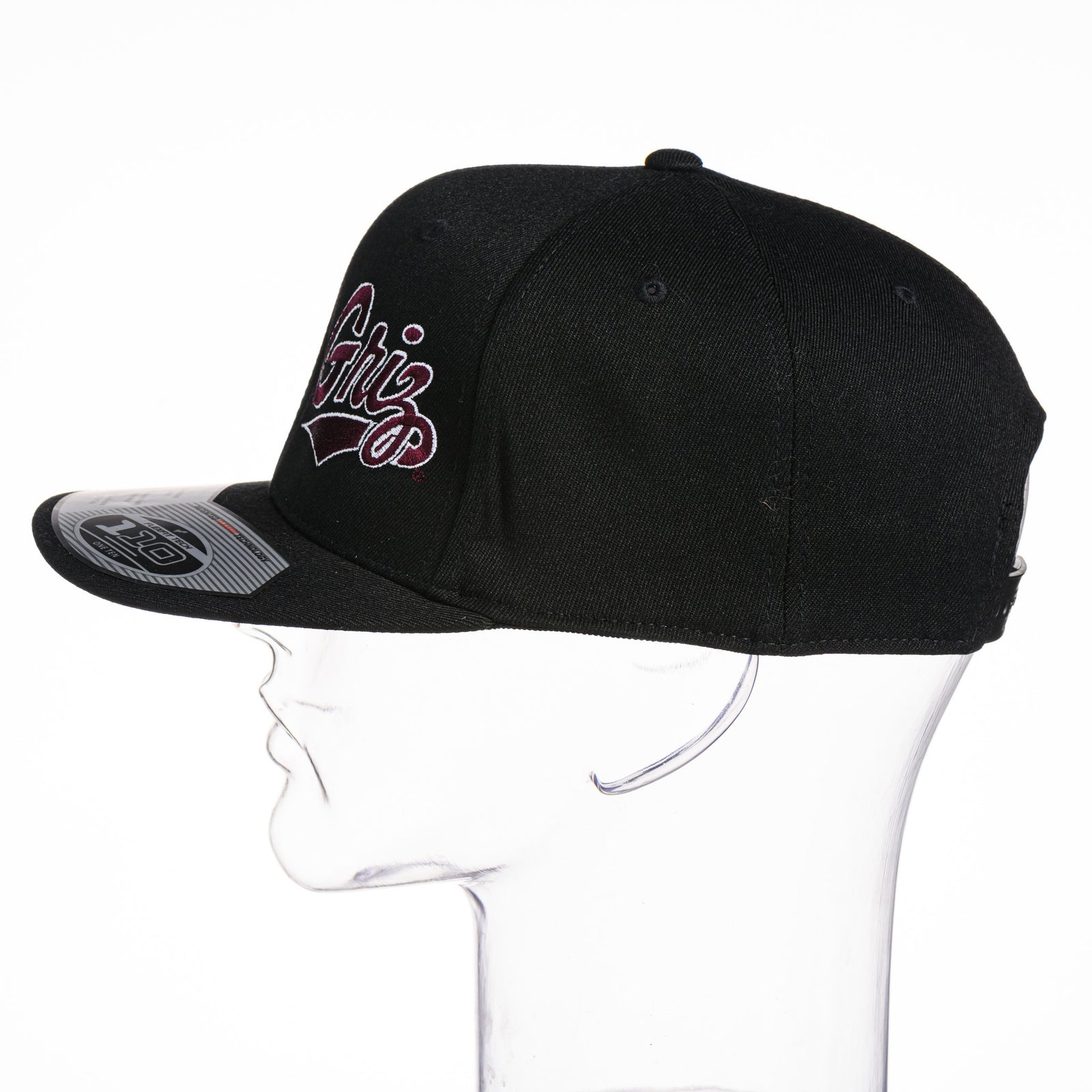 Black Outlined Griz Script - Flexfit Flat Bill Hat made in Missoula, MT (home of the UM Grizzlies) by Blue Peak Creative—a black flat bill hat embroidered with the outlined maroon University of Montana Griz script (side view).
