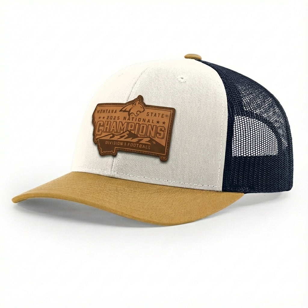 This is a mid-profile Richardson 112 trucker cap with a smooth cream fabric front, a breathable navy mesh back, and a stiff amber gold curved brim. The front features a textured, genuine leather patch with deep, laser-etched recessed lettering and designs. The patch is firmly bonded to the fabric and finished with a smooth, protective sealant. It is secured with an adjustable plastic snapback at the rear.