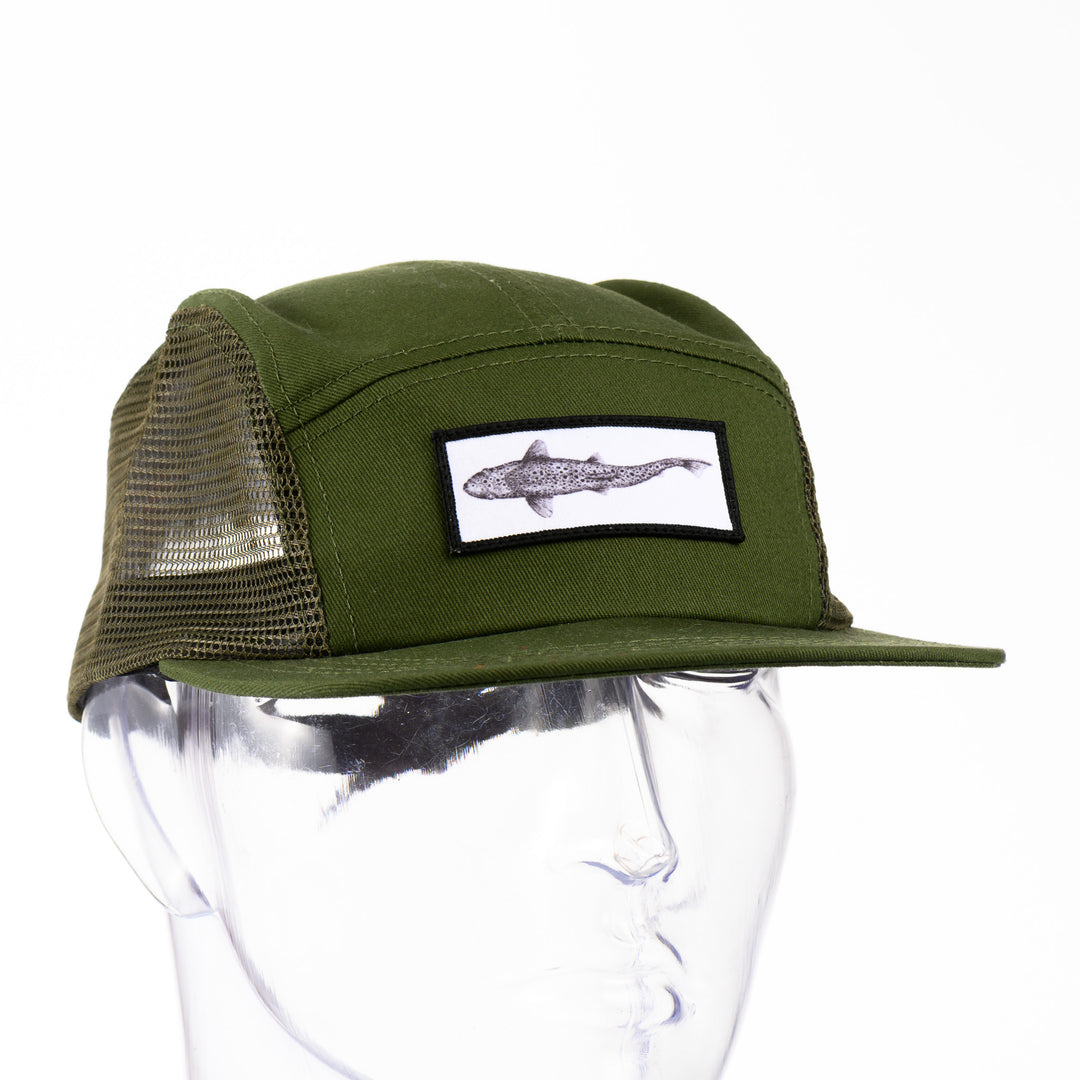Front of a green adjustable mesh-sided cap with a patch featuring original black and white artwork by Brittany Finch -  a swimming brown trout viewed from above -  made in Montana by Brittany Finch Art and displayed on a mannequin head 