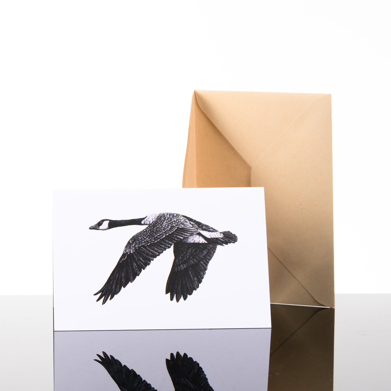 Blank greeting card featuring original black and white artwork by Brittany Finch - a Canadian goose, mid-flight - and kraft brown envelope by Brittany Finch Art in Montana