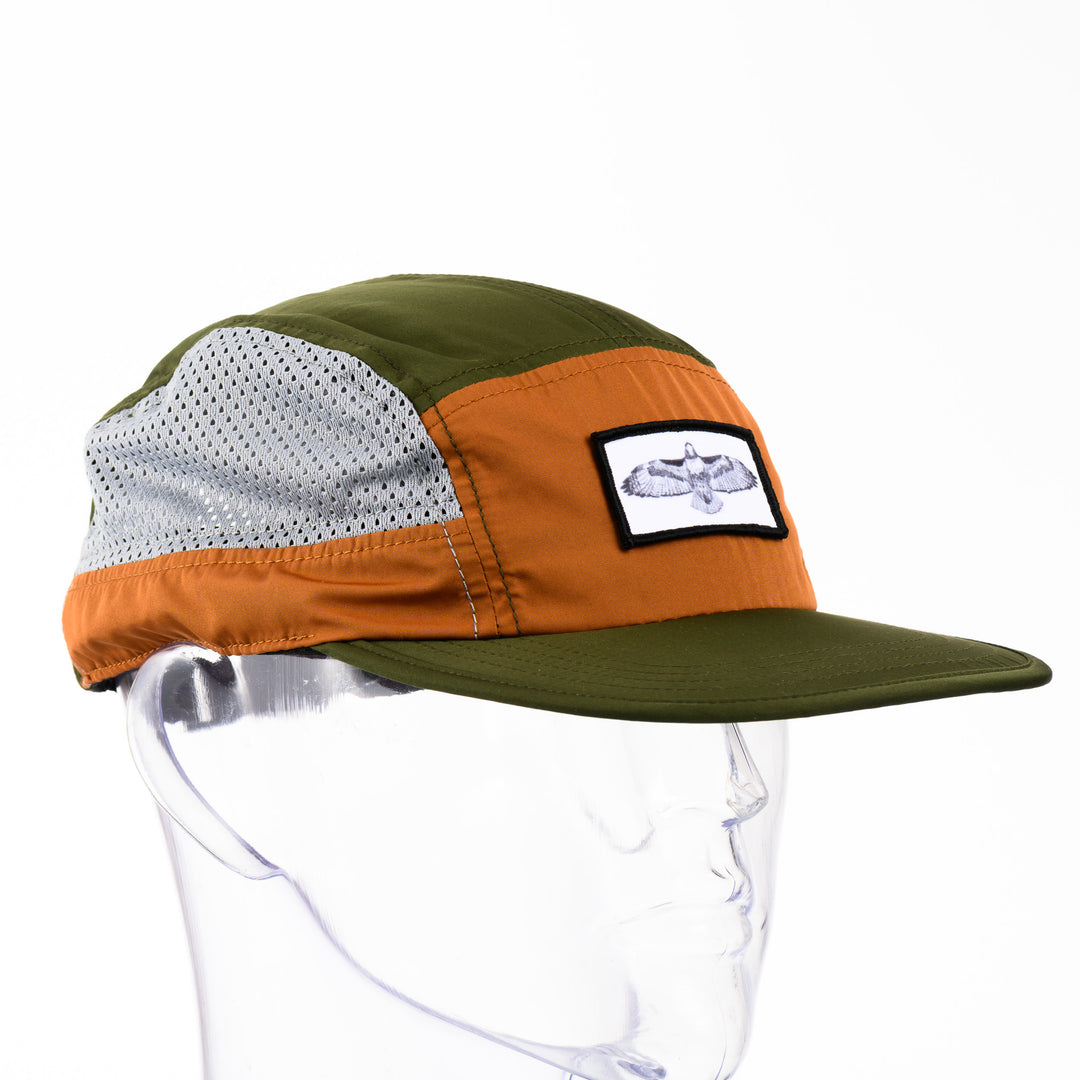 3/4 view of a green and orange adjustable mesh-sided cap with a patch featuring original black and white artwork by Brittany Finch -  a soaring red tailed hawk, wings outstretched -  made in Montana by Brittany Finch Art and displayed on a mannequin head 