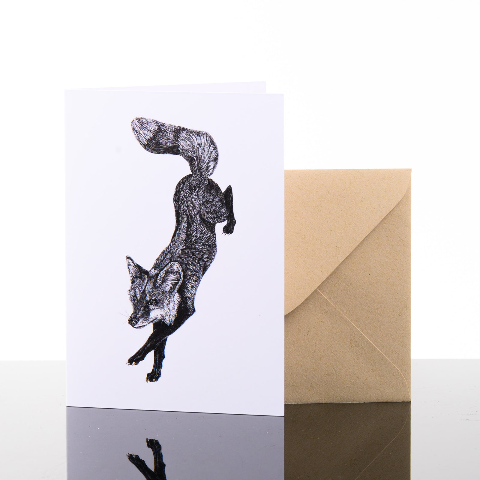 Blank greeting card featuring original black and white artwork by Brittany Finch - a dynamic red fox, on a descending leap - and kraft brown envelope by Brittany Finch Art in Montana