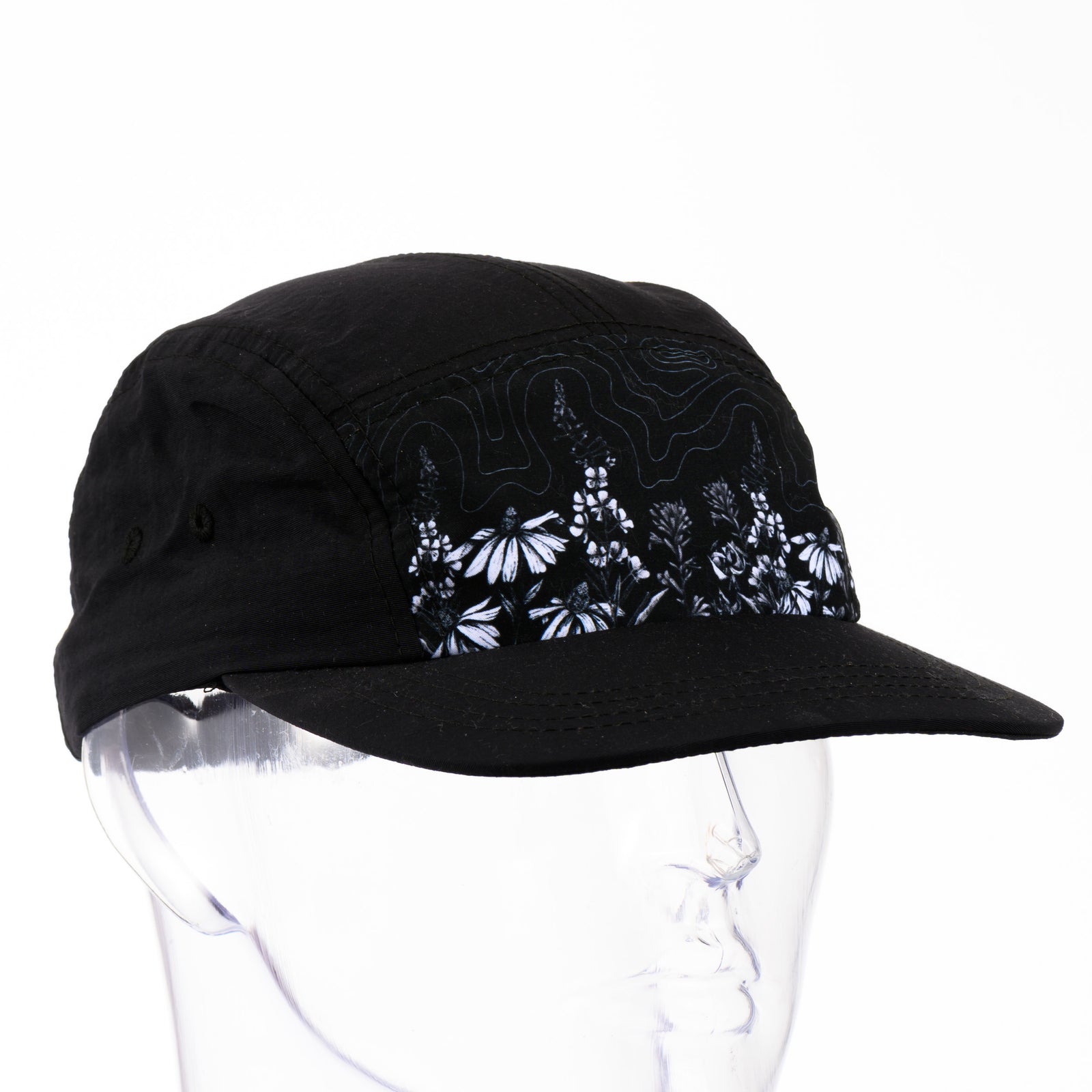 3/4 view of a black 5-panel hat with a brim featuring original black and white artwork by Brittany Finch -  wildflowers stretched across the front panel -  made in Montana by Brittany Finch Art and displayed on a mannequin head 