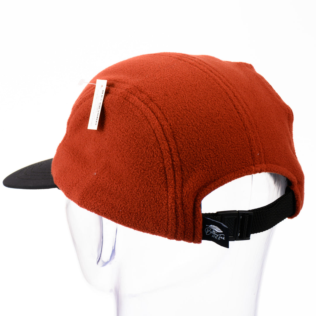 Back of an orange and black fleece 5-panel hat with a brim and a patch featuring original black and white artwork by Brittany Finch -  a bear sitting on its haunches -  made in Montana by Brittany Finch Art and displayed on a mannequin head 