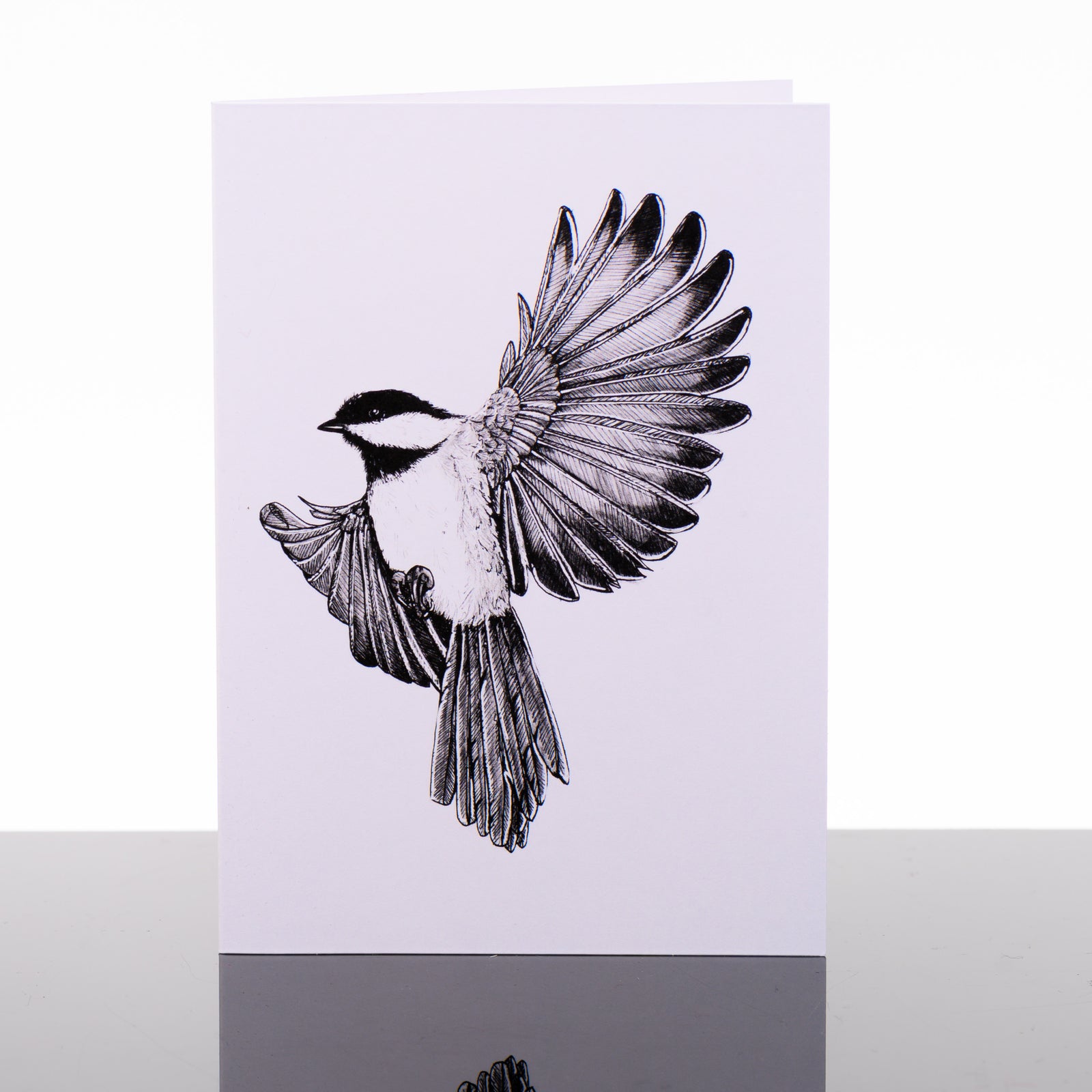 Blank greeting card featuring original black and white artwork by Brittany Finch - a Black-capped Chickadee, arrested mid-air with wings spread wide - by Brittany Finch Art in Montana