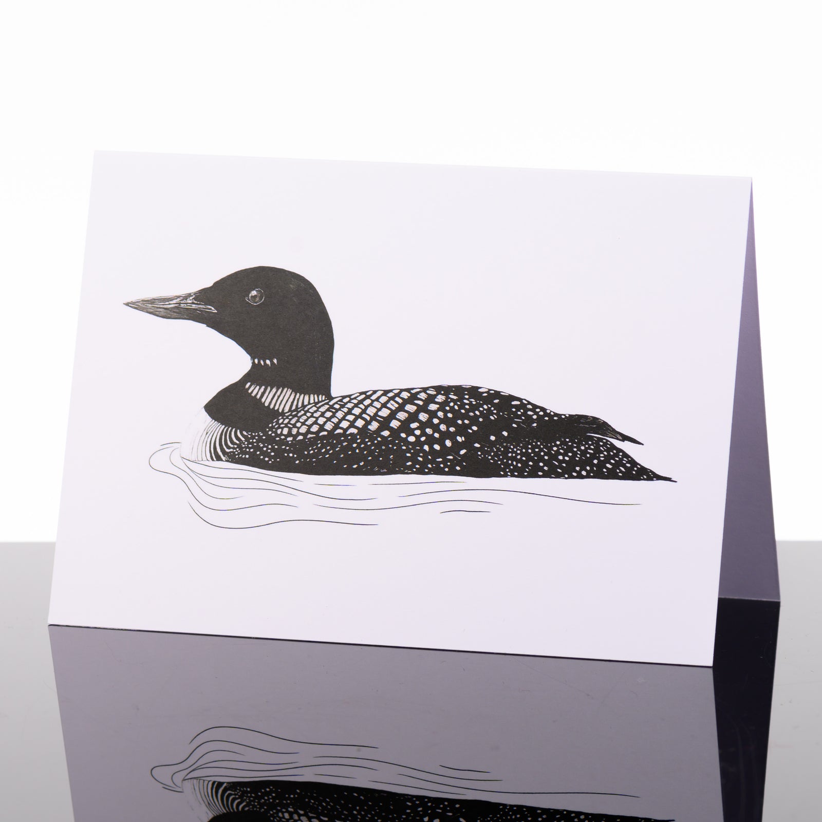 Blank greeting card featuring original black and white artwork by Brittany Finch - a loon floating in rippling water - made in Montana by Brittany Finch Art