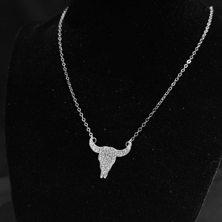 A sterling Silver buffalo skull pendant necklace made by Cobblestone Designs of Montana on a black background with a silver chain.