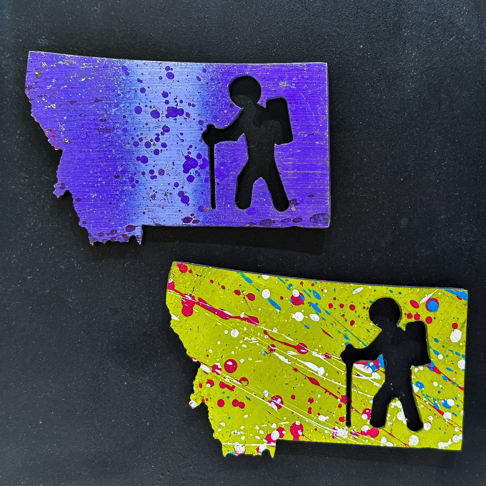 A made in Montana state-shaped cut-out with silhouettes of hikers embedded in it and a strong back magnet. Design 1.