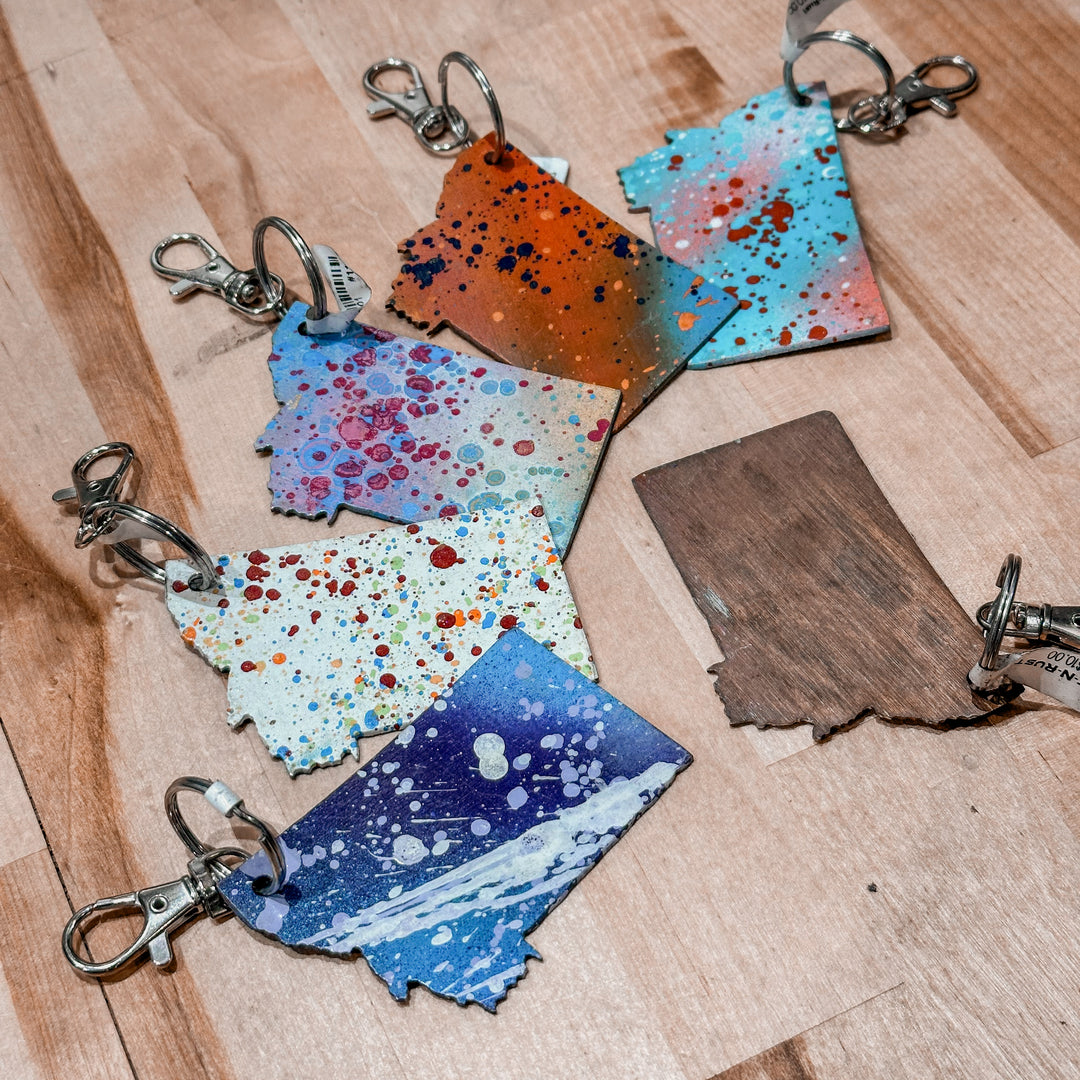 This made in Montana Metal Keychain showcases a state-shaped design with various paint splatter colors