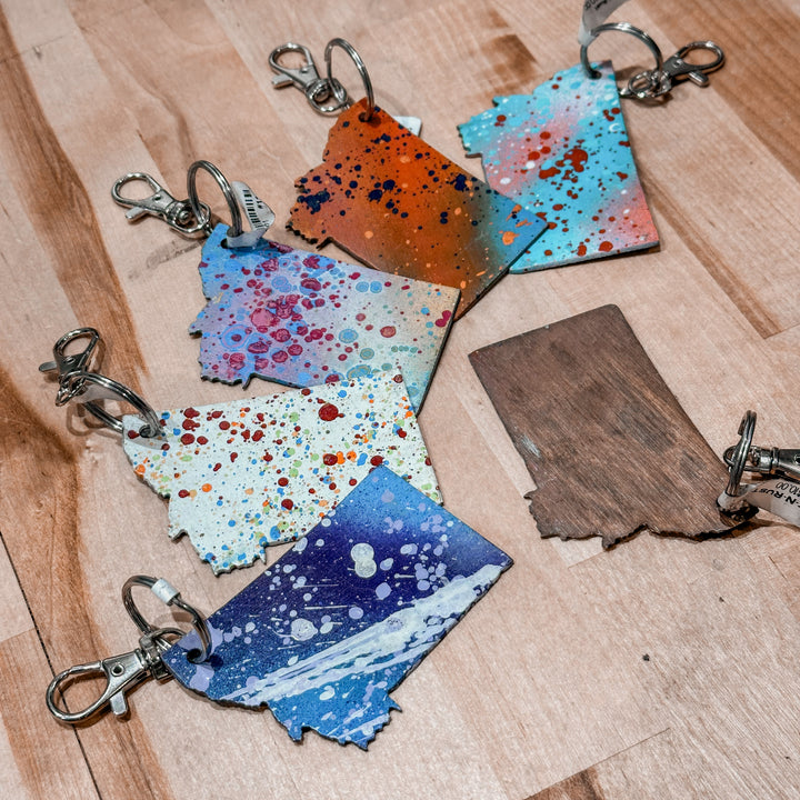 This made in Montana Metal Keychain showcases a state-shaped design with various paint splatter colors