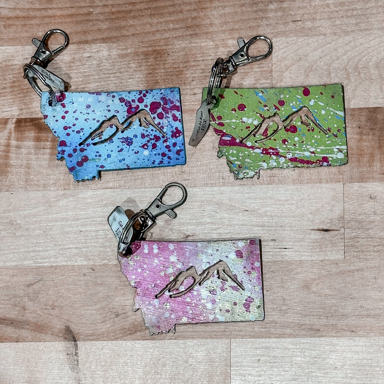 These made in Montana metal keychains are the shape of Montana with mountains cut out and feature a colorful splash of paint.