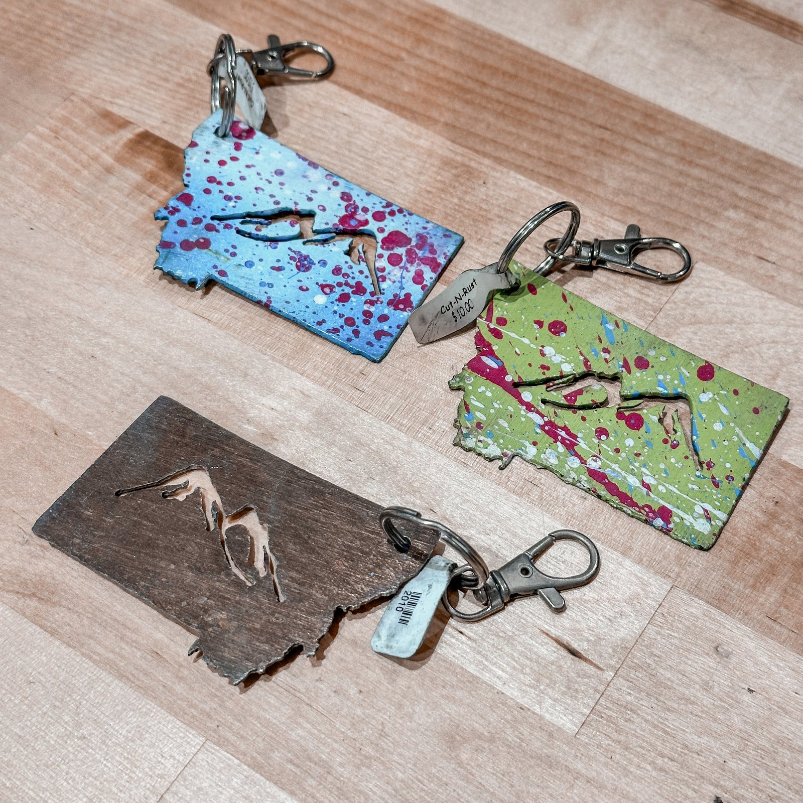 These made in Montana metal keychains are the shape of Montana with mountains cut out and feature a colorful splash of paint.