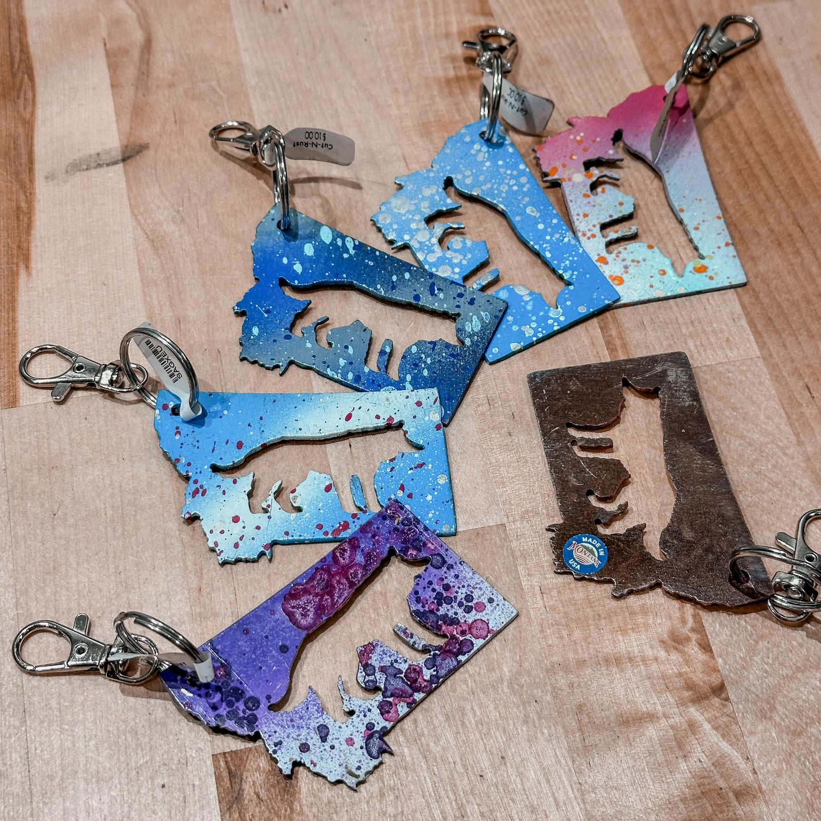 This Montana made  Wolf Metal Keychain showcases a state-shaped design with a wolf silhouette cut out of it.