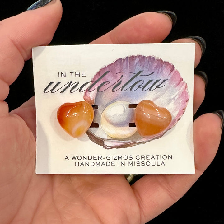 Card with shell and heart-shaped carnelian stones on a hand, featuring &