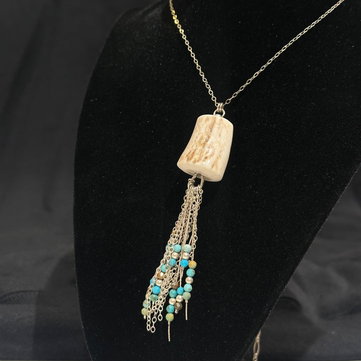An artisinal necklace made of antler, silver chain and turquoise beads on a black background.