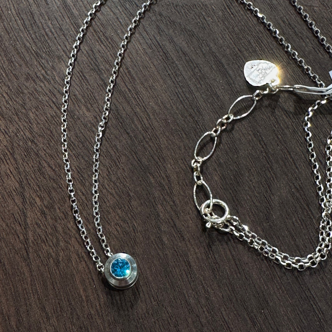 A cubic zirconia gemstone colored glittering Topaz Blue for a December Birthstone Necklace, set in sterling silver on a dark wood background