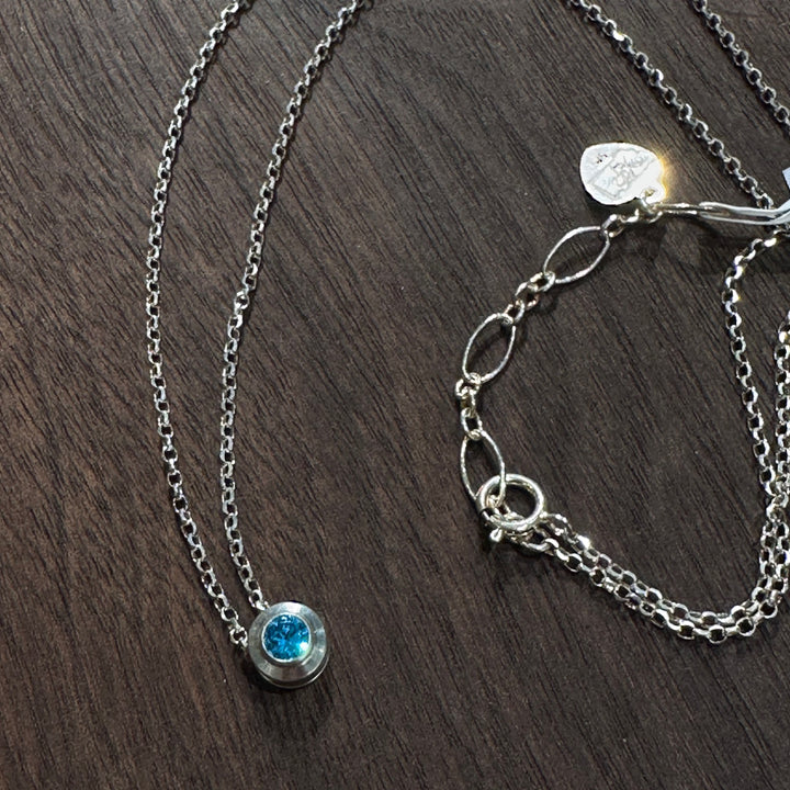 A cubic zirconia gemstone colored glittering Topaz Blue for a December Birthstone Necklace, set in sterling silver on a dark wood background