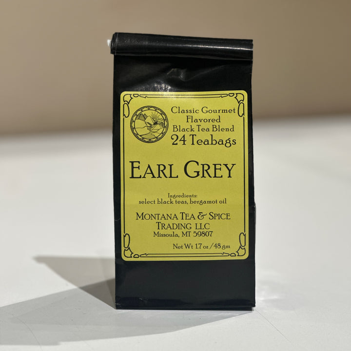 A black stand-up pouch of Earl Grey tea with a large yellow label, photographed on a light surface against a beige background. The label reads Classic Gourmet Flavored Black Tea Blend, 24 Teabags, and shows Montana Tea &amp; Spice Trading LLC.