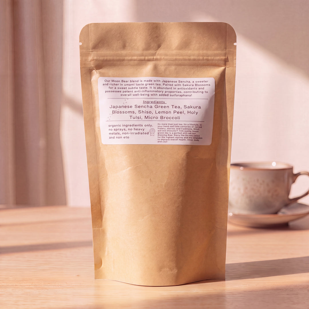 A stand-up kraft paper pouch of tea on a wooden table with a blurred teacup in the background. The front label reads &
