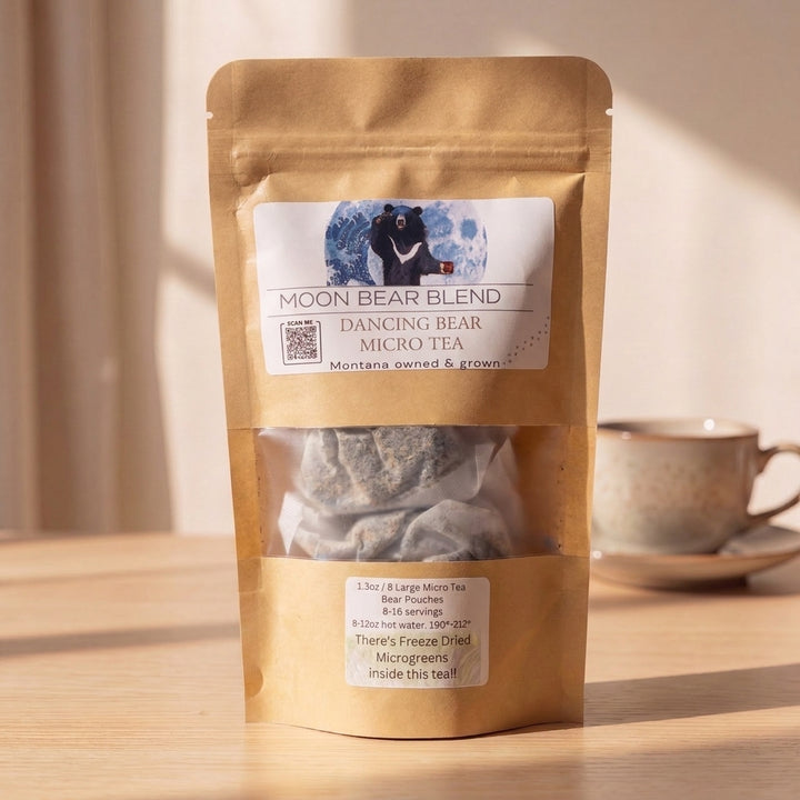 A stand-up kraft paper pouch of Moon Bear Blend Dancing Bear Micro Tea stands on a wooden table in warm sunlight, with a teacup blurred in the background.