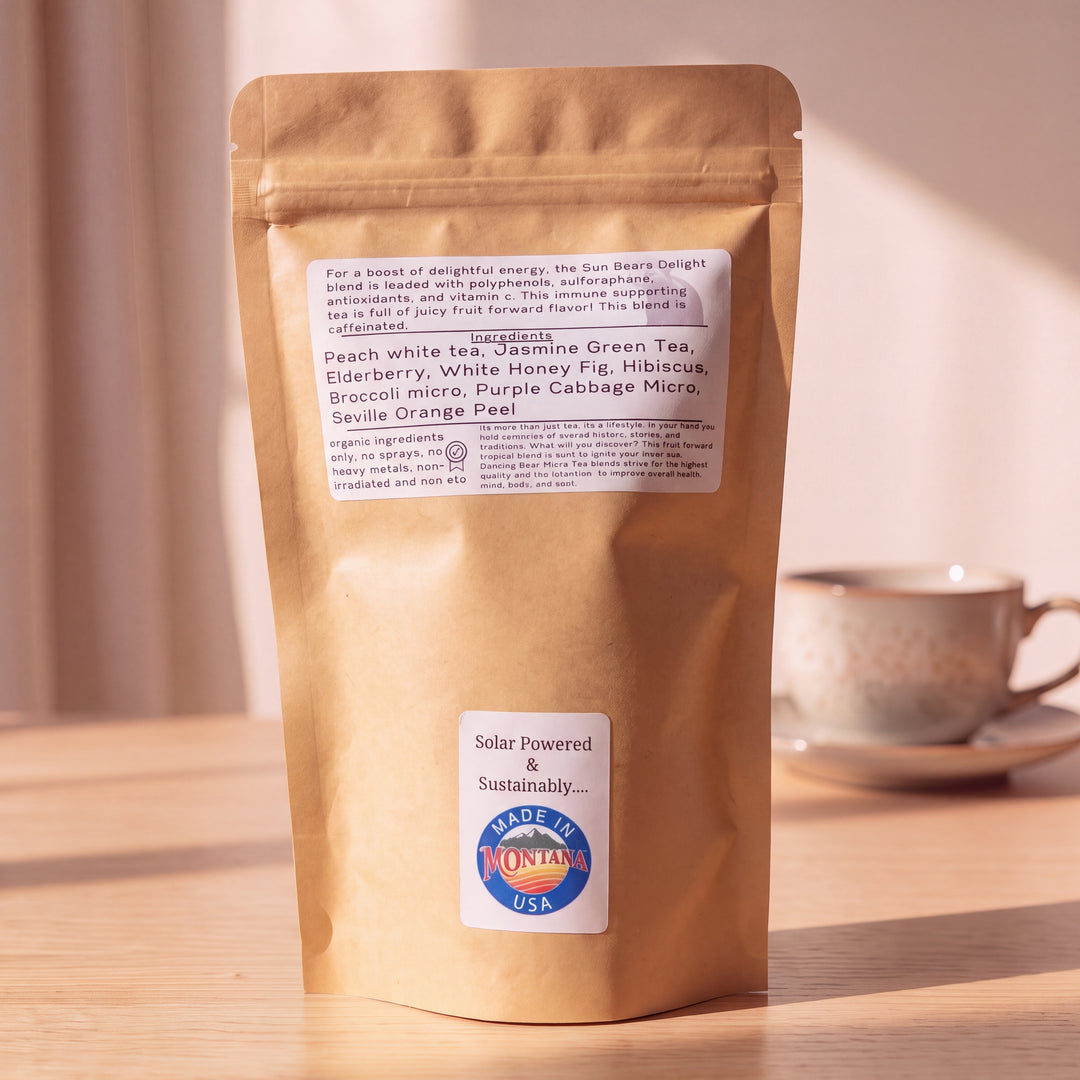 A kraft paper stand-up pouch of tea sits on a wooden surface with a blurred tea cup in the background. The pouch has a white ingredient label and a lower white sticker that reads &