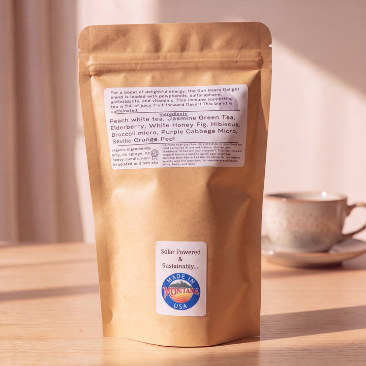 A kraft paper stand-up pouch of tea sits on a wooden surface with a blurred tea cup in the background. The pouch has a white ingredient label and a lower white sticker that reads &
