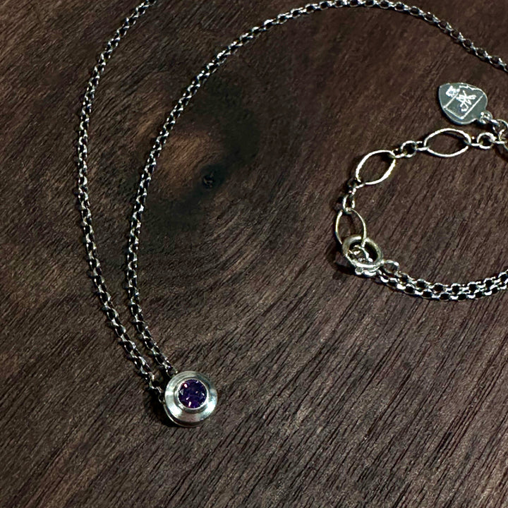 A cubic zirconia gemstone colored deep amethyst purple for a February Birthstone Necklace, set in sterling silver on a dark wood background